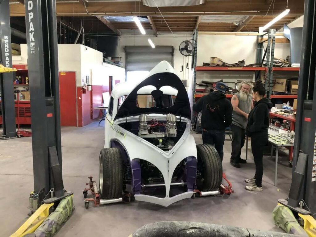 A custom car is being worked on at Gotham Garage, with two customers talking to shop owner Mark Towle nearby.
